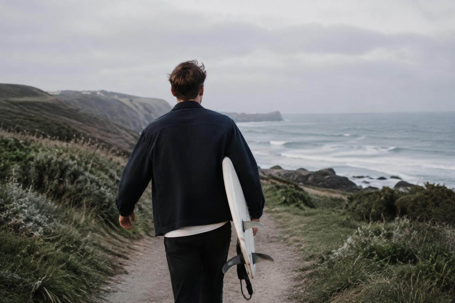 A person carrying a surfboard along a coastal path